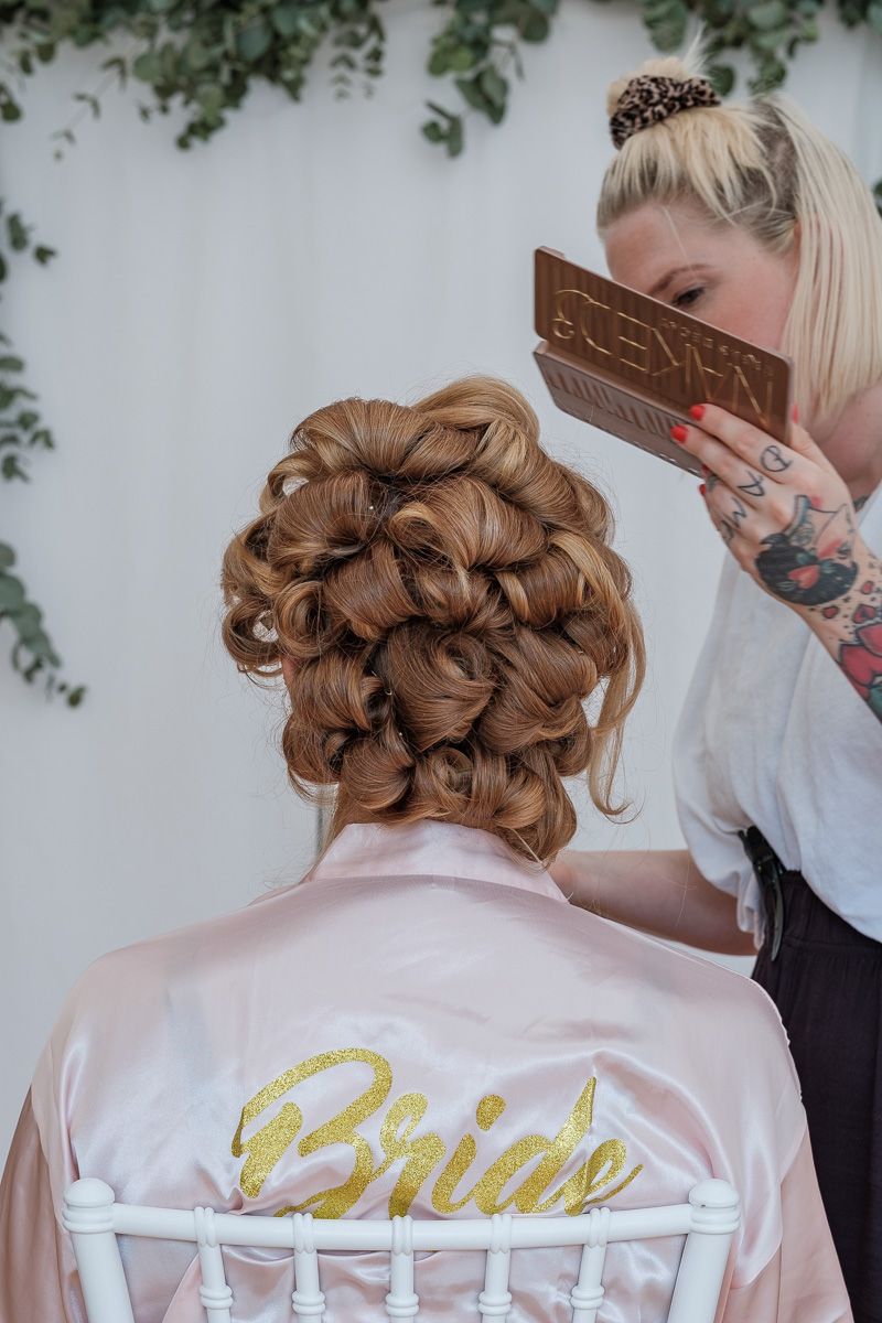 Anna im Morgenmantel mit dem Schriftzug Bride, an ihrer Hochsteckfrisur wird noch gearbeitet