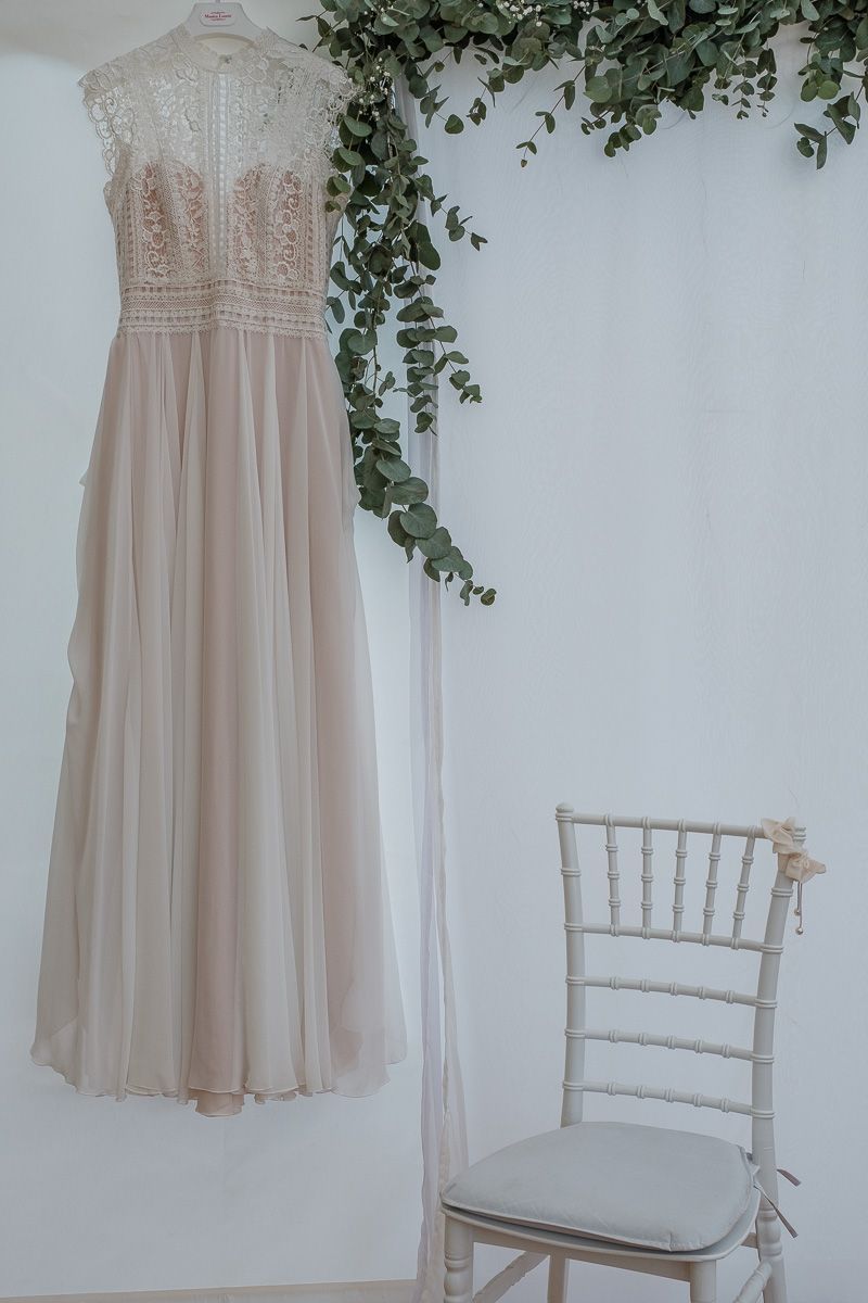 Das Brautkleid hängt an einer Wand mit Eukalyptusranken, daneben ein weißer Stuhl